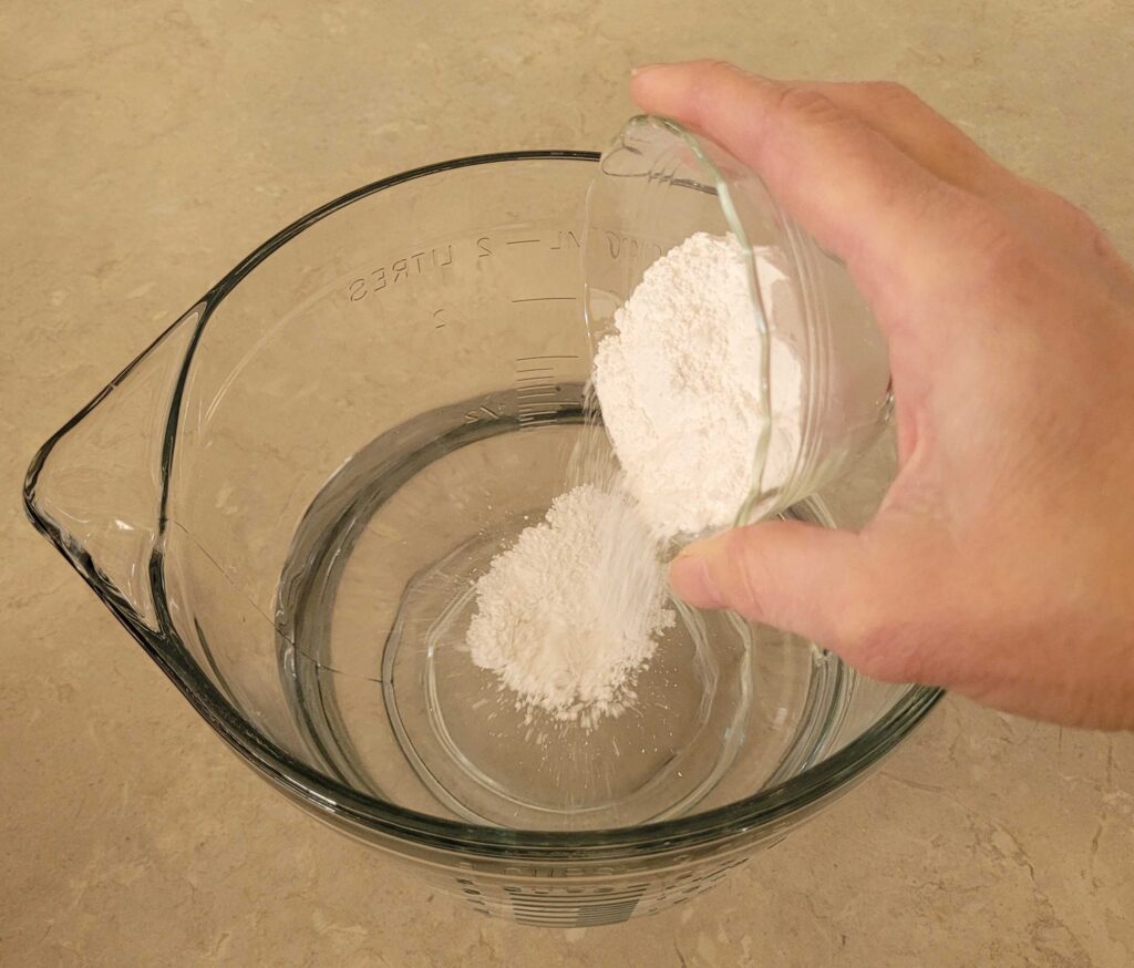hand pouring white powdered lime into measuring bowl of water
