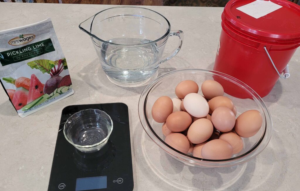 bag of pickling lime, measuring cup of water, red bucket with lid, bowl of eggs, scale with small dish
